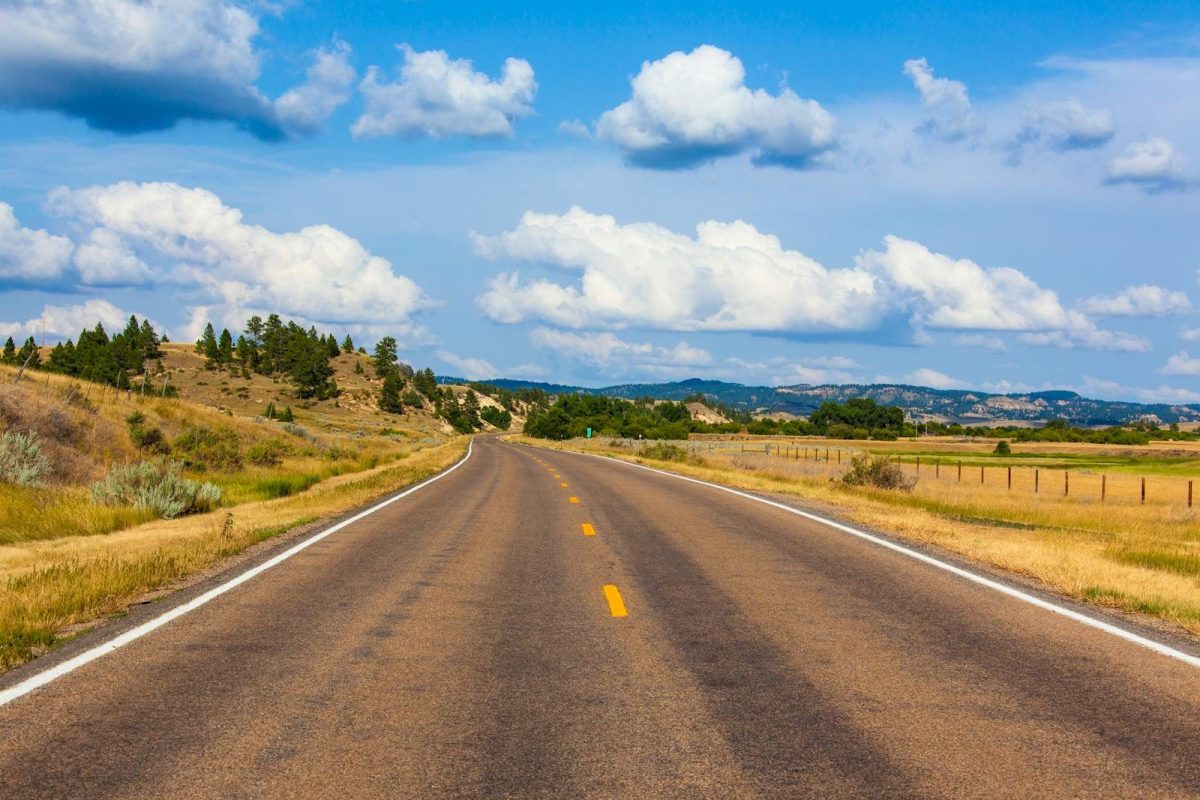 A picturesque highway stretches through Montana, surrounded by rolling landscapes and a clear blue sky.