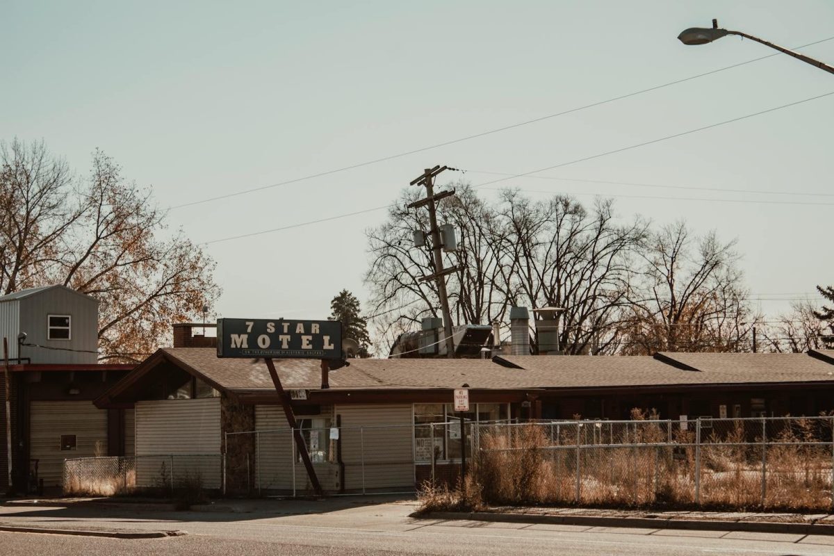 A vintage 7 Star Motel with a prominent sign, surrounded by tall grass and fencing, under a clear sky.