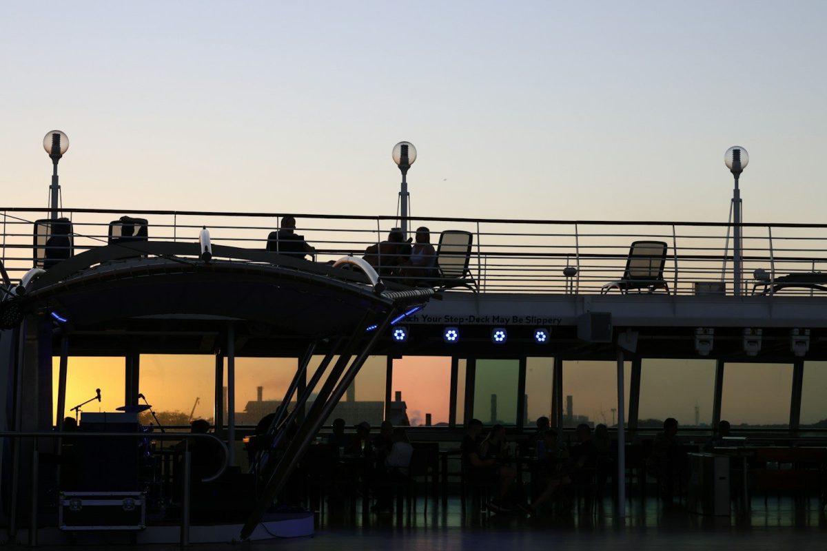 Silhouetted boat with people reflecting sunset in windows.