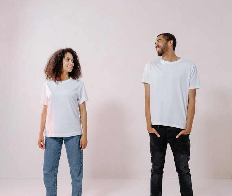 A man and woman wearing white shirts stand smiling in a bright studio.