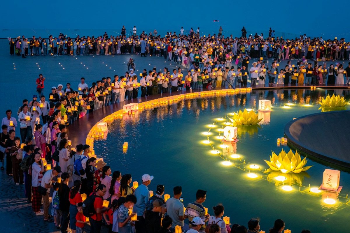 Crowd releasing illuminated lanterns on water at dusk
