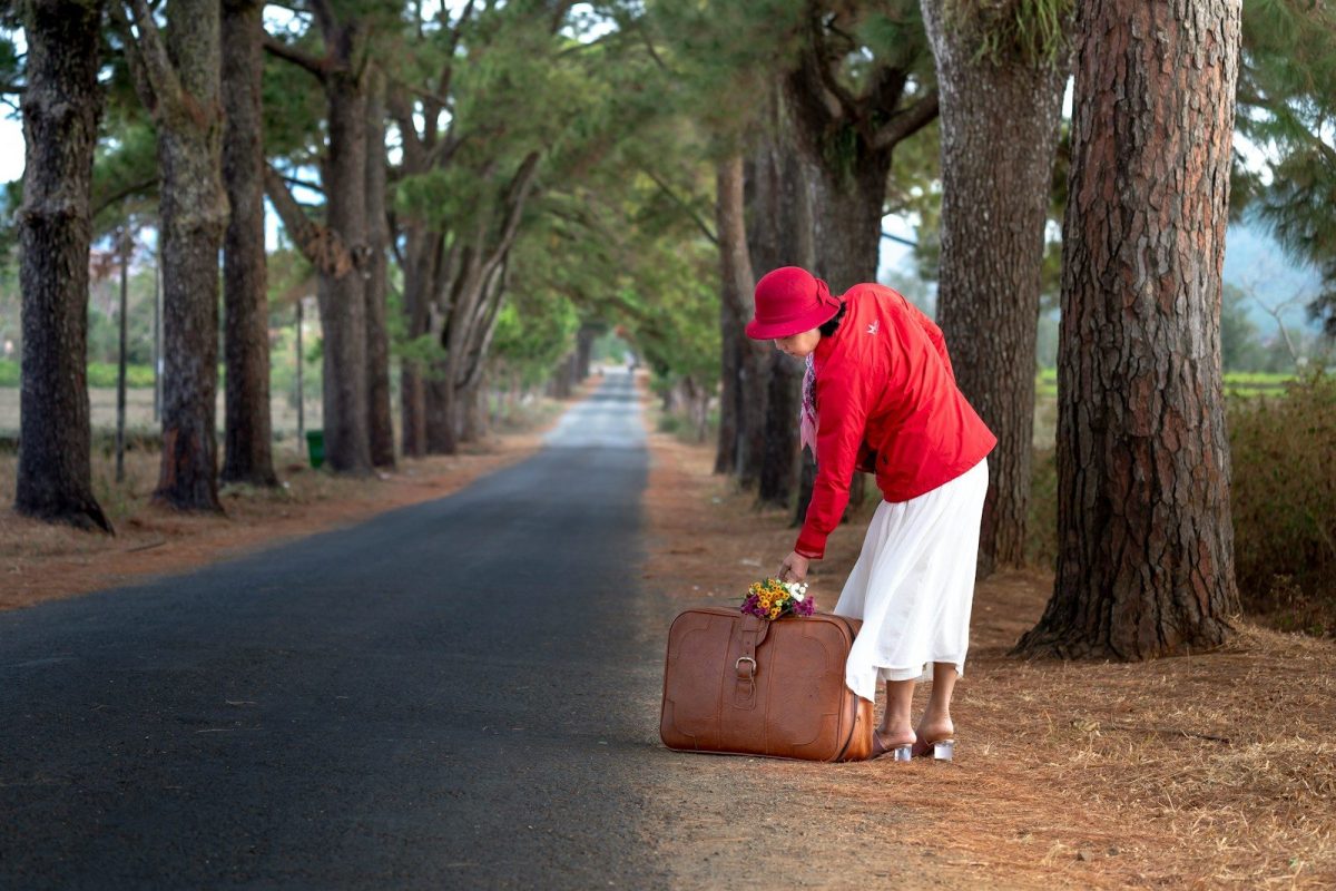 A woman in a red jacket and white skirt with a brown suitcase