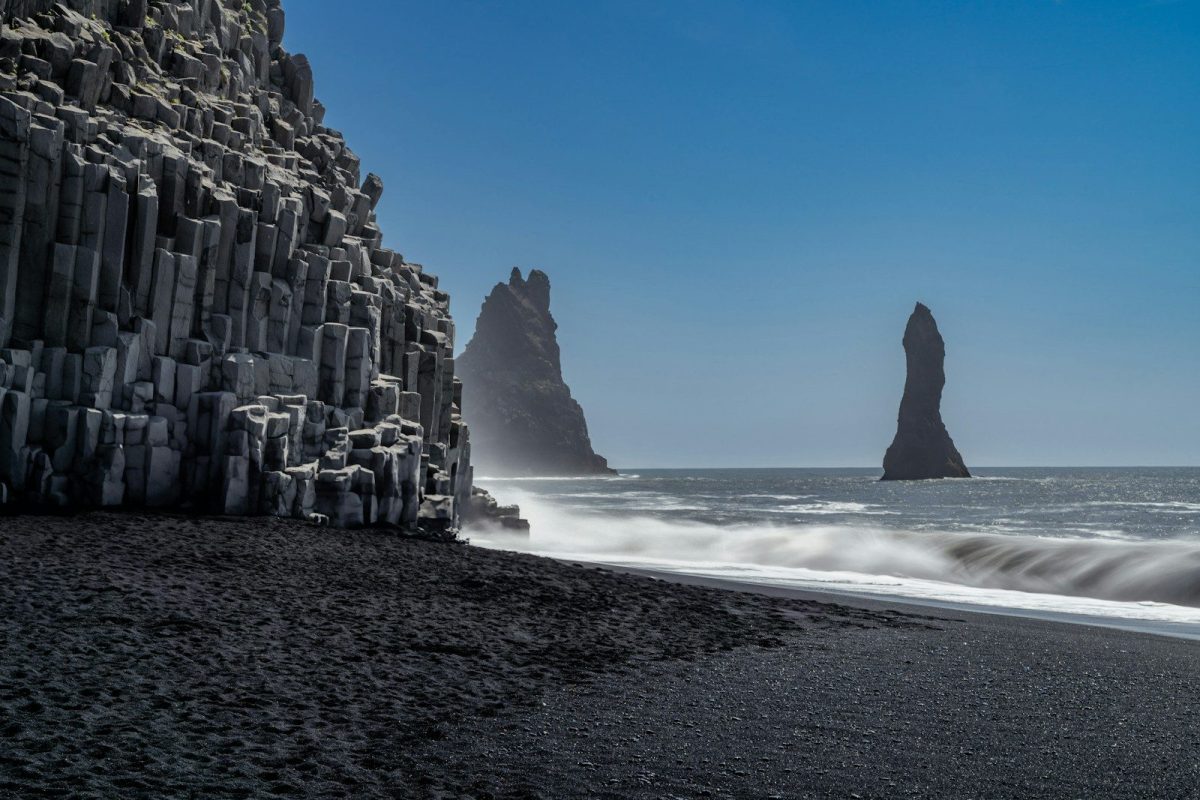A black sand beach with a rock formation in the background