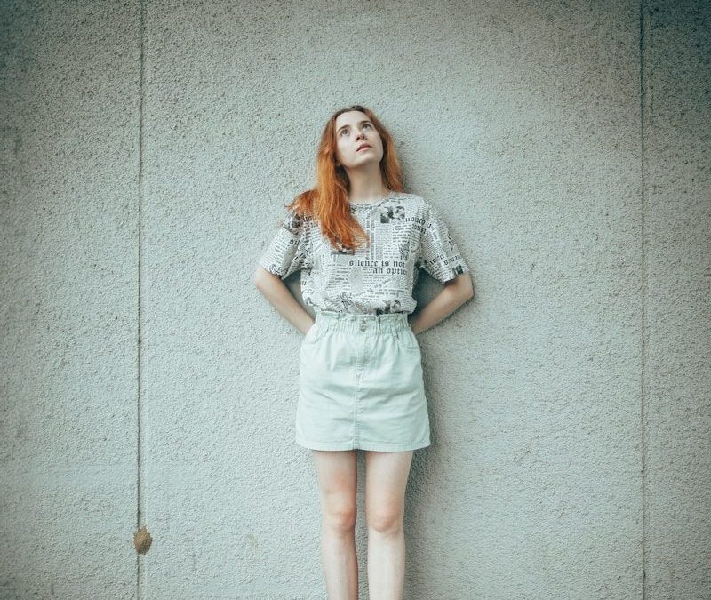 Young woman with red hair looking up against wall