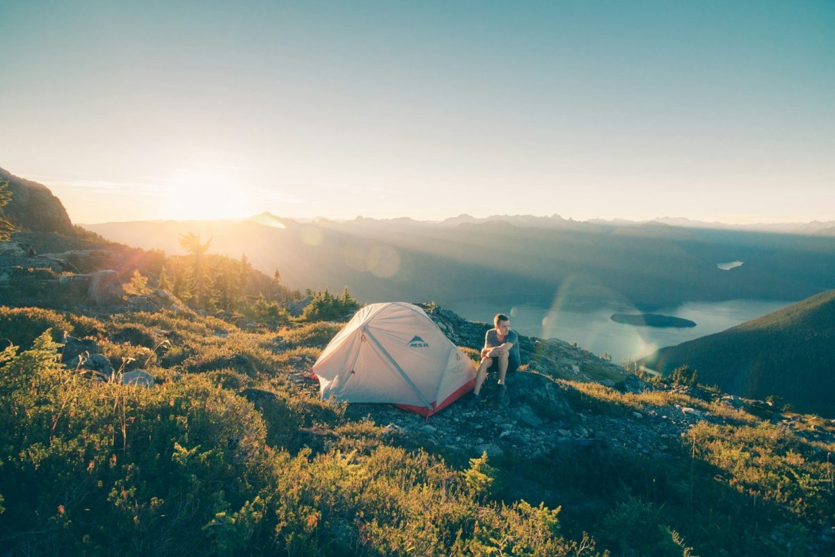 8 Ways to Stay Warm and Comfortable While Traveling in the Wilderness 4 man sitting on stone beside white camping tent