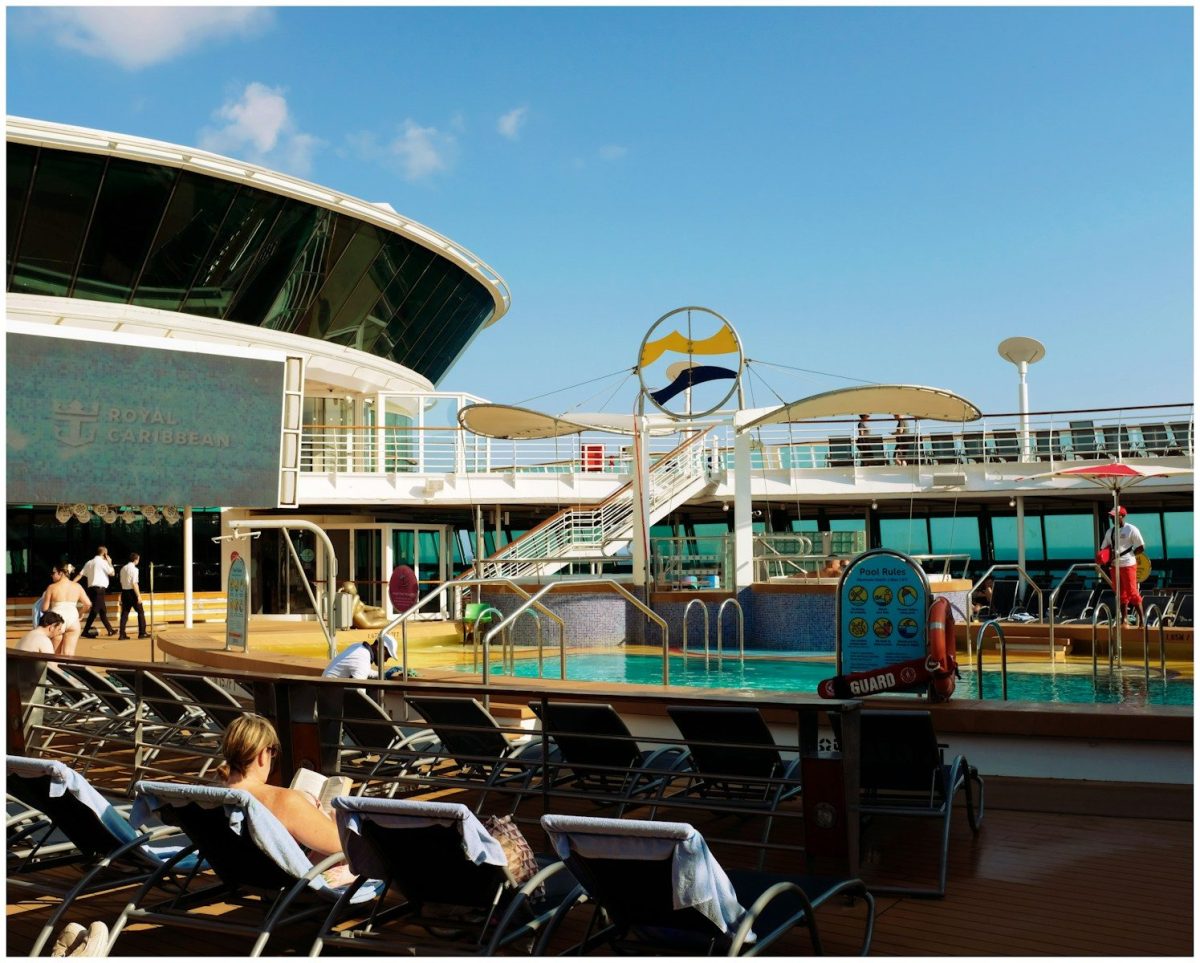 People relaxing on lounge chairs by a cruise ship pool.