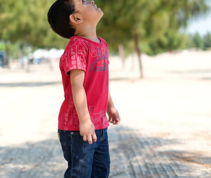 girl in red shirt and blue denim jeans standing on gray concrete road during daytime