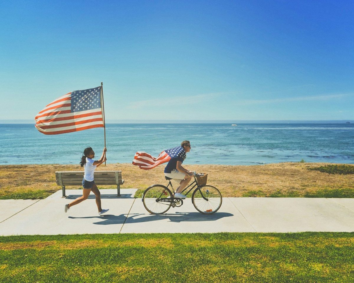 8 Reasons Some European Travelers Are Rethinking U.S. Trips 7 man riding bike and woman running holding flag of USA