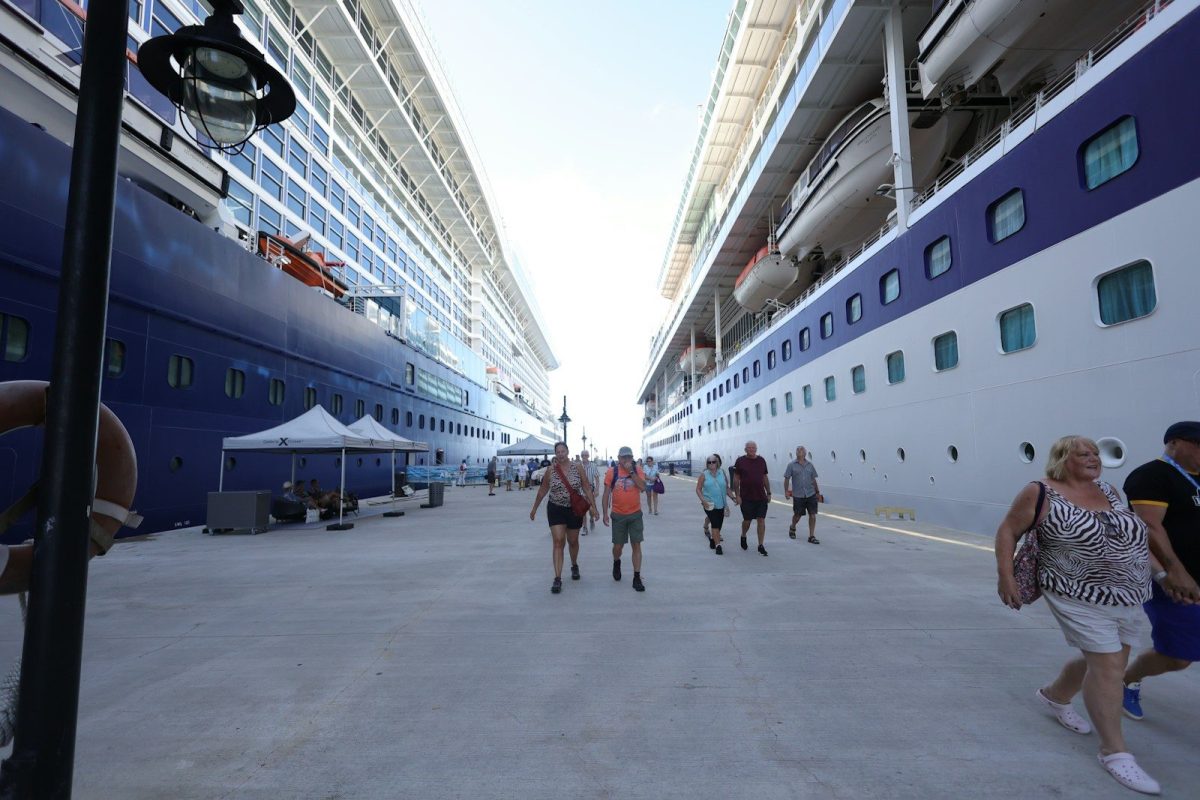 People walk on a pier between two large cruise ships.