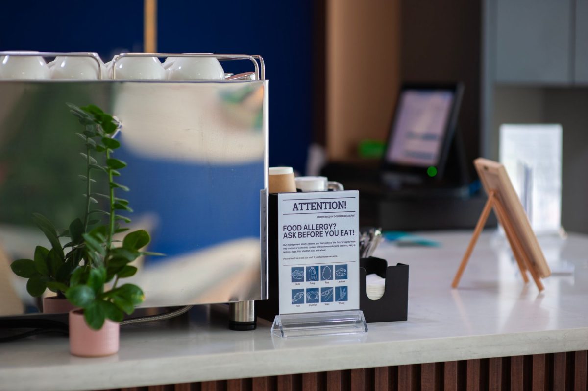 5 Hotel Breakfast Rules Families Should Check Before Leaving the Room 5 Coffee shop counter featuring an allergy warning sign and plant, highlighting food safety.