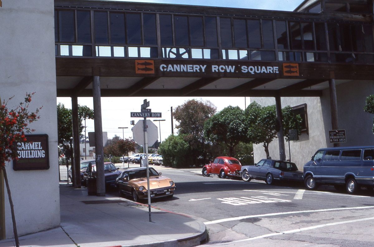 Classic cars parked under the Cannery Row Square bridge in a vintage street scene.