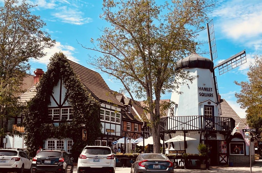 Quaint European style village scene featuring a windmill and classic architecture under a blue sky.