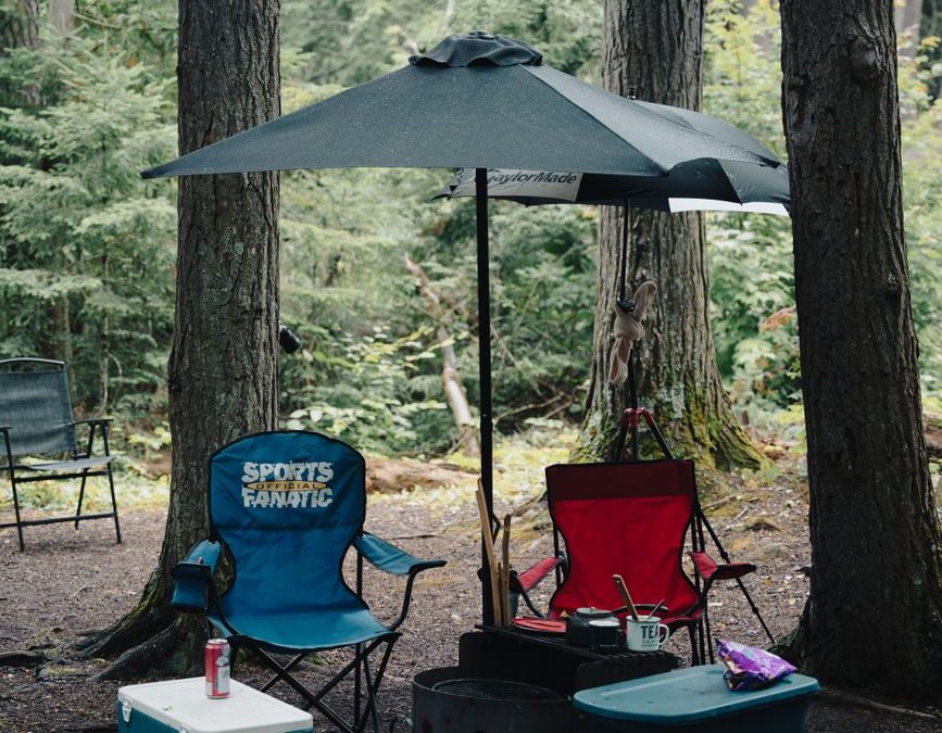 5 Campground First-Night Checks Travelers Usually Wish They Did Before Dark 2 A cozy camping setup in the forest with chairs, a cooler, and an umbrella.