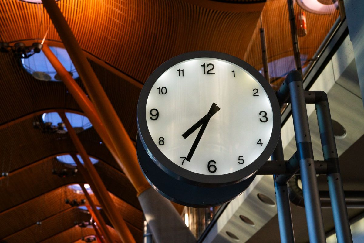 A large clock displaying one o&amp;#39;clock inside a modern airport terminal with a curved ceiling.