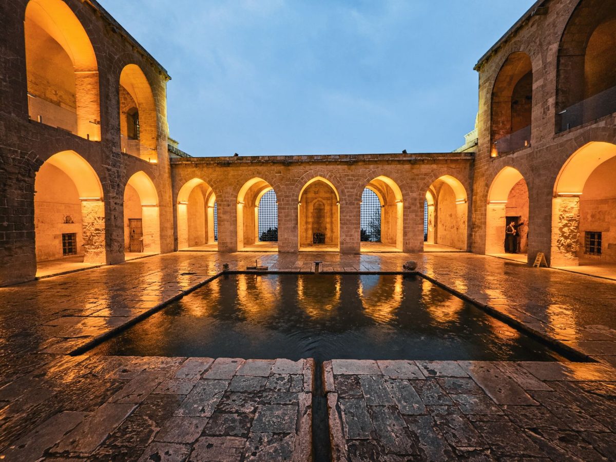 A serene twilight view of an ancient courtyard in Mardin, Türkiye, with illuminated arches.