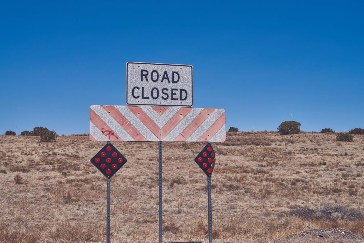 Road closed sign in a dry, desert setting under a clear blue sky, symbolizing detour or restriction.