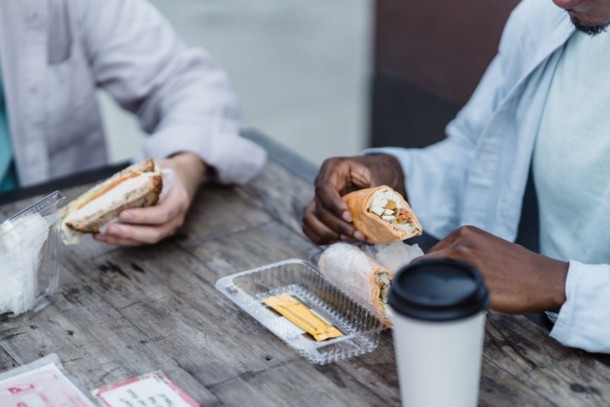 5 Airport Food Habits Frequent Flyers Use to Avoid Regret 3 Two friends enjoying wraps and sandwiches at a rustic outdoor wooden table, sharing a casual lunch.
