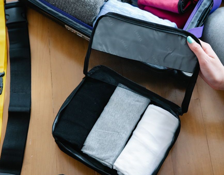 A person efficiently packs clothing and essentials into a suitcase for travel, showcasing organization and preparation style.