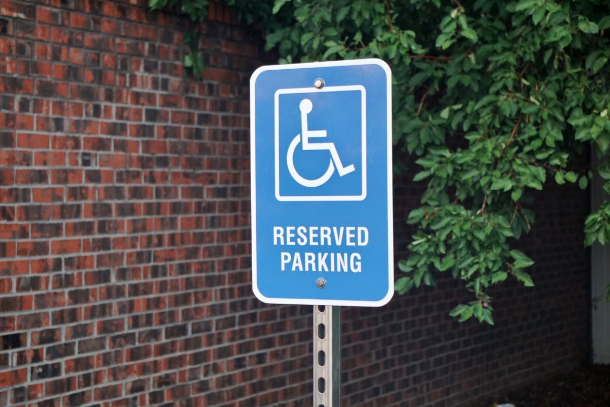 Blue sign indicating reserved parking space for disabled access by a brick wall.