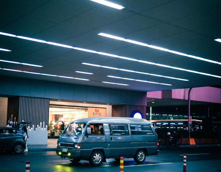 A vibrant urban evening scene featuring a van by a modern storefront under neon lights.