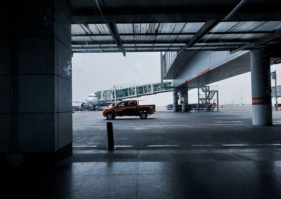 A red pickup truck parked at the terminal entrance of Kolkata Airport, with a clear view of an airplane.