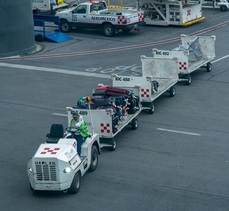 Ground crew managing luggage on tarmac with baggage carts and vehicle at airport.