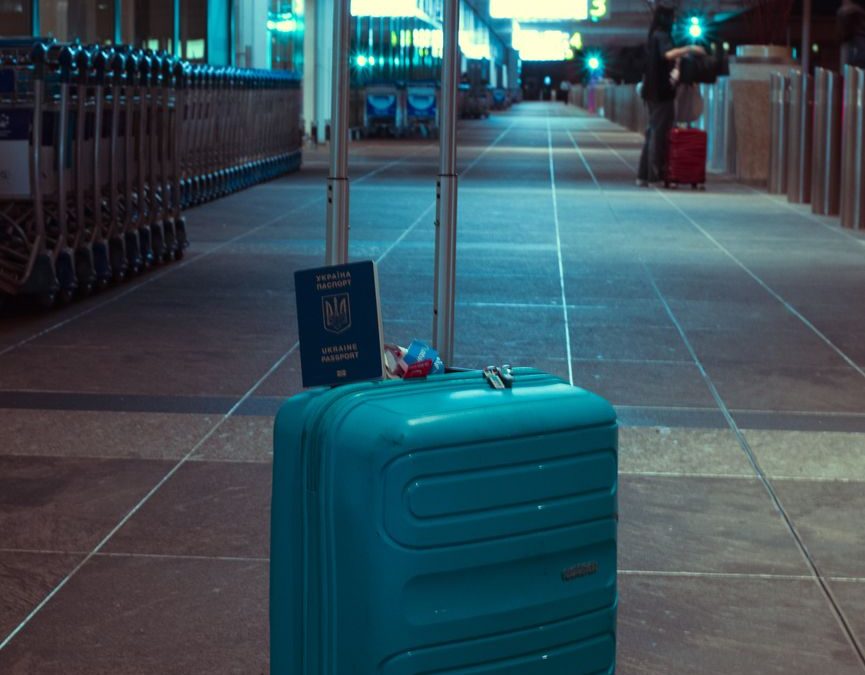 A blue suitcase with a passport in an empty airport terminal at night.