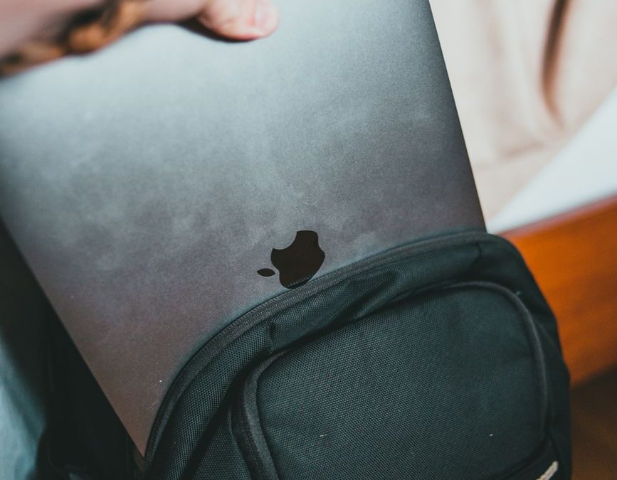 A close up of a person placing a laptop into a black backpack indoors.