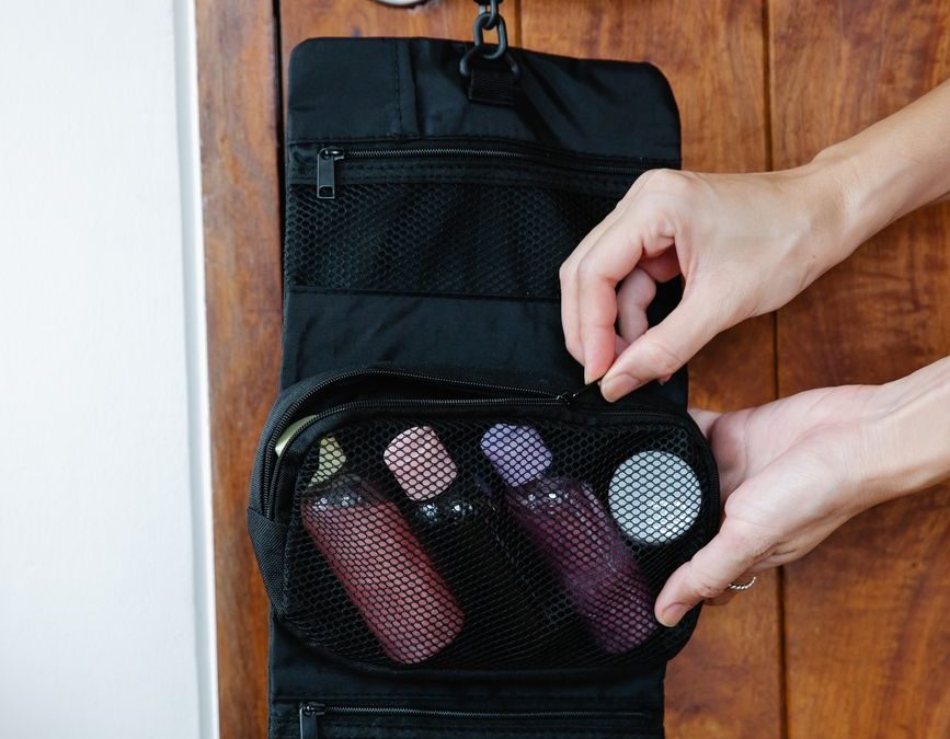 Travel toiletry bag organized with cosmetics, hanging on a wooden door handle.