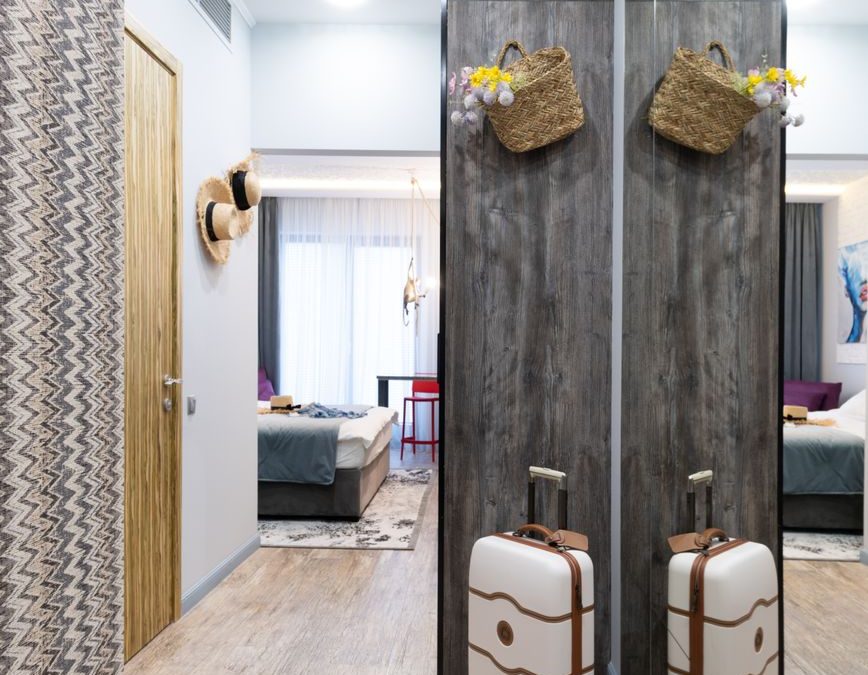 Luggage placed near wall in long corridor of modern hotel room with decoration on wall and bedroom in distance during travelling