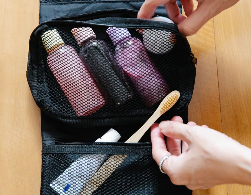 Open toiletry bag with bottles and a bamboo toothbrush on wooden surface.