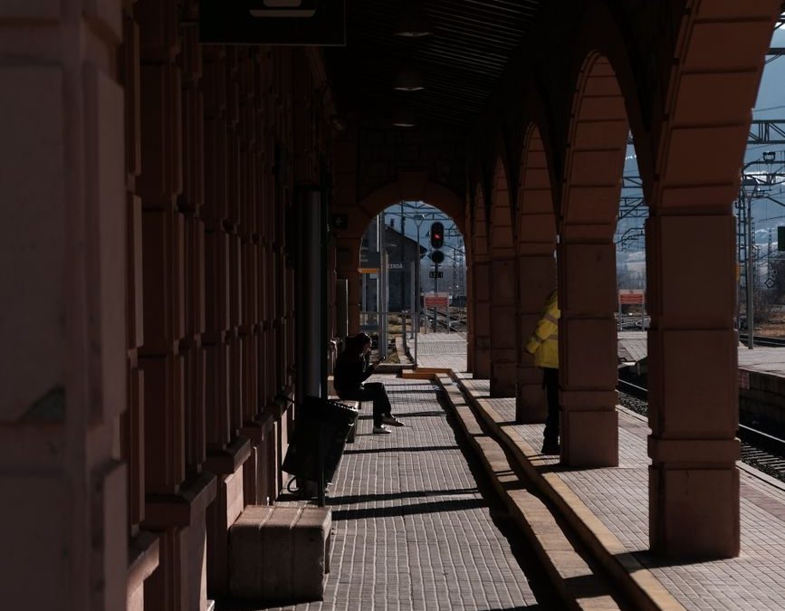 A sunlit hallway with arches at a train station, casting dramatic shadows.
