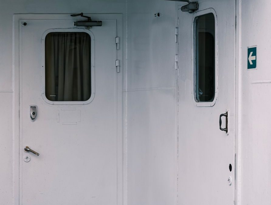 Minimalist photo of a ship&amp;#39;s interior featuring white doors and a directional sign.