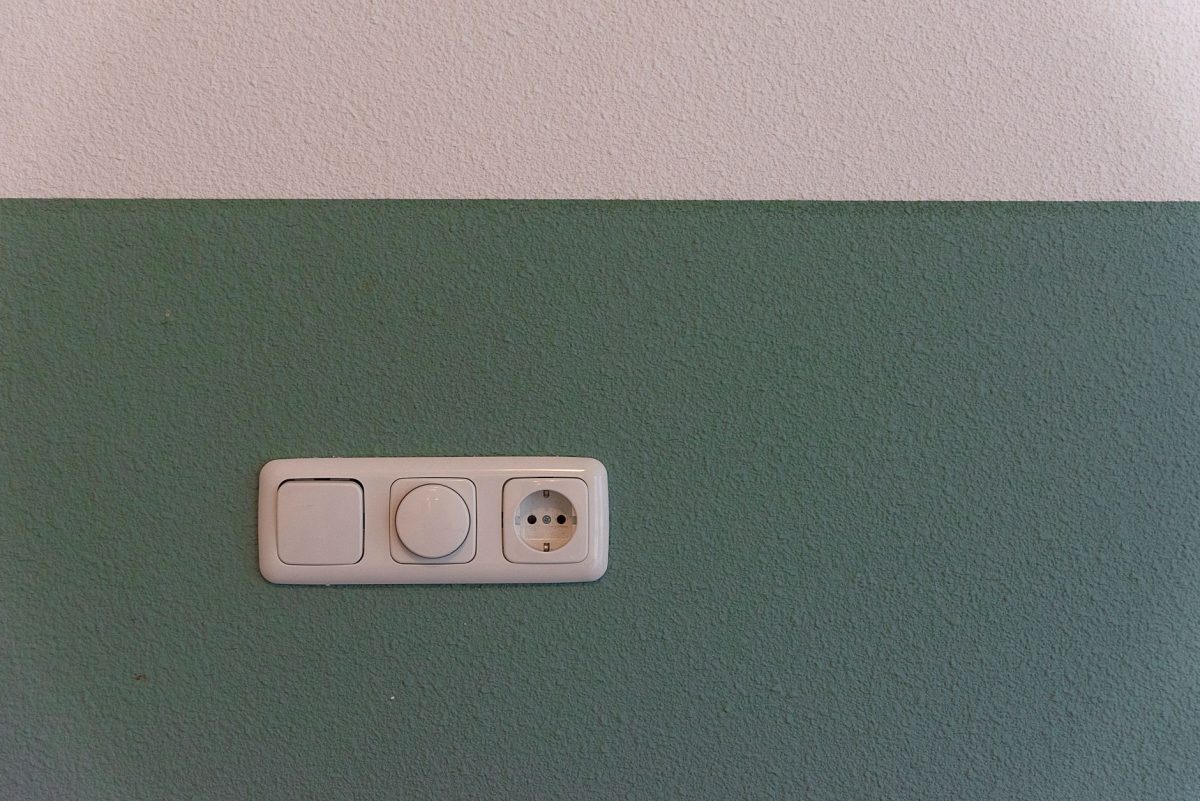 Close up of a power outlet and switch on a textured green wall indoors.