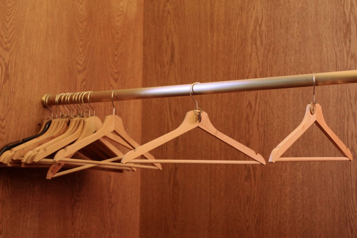A row of wooden hangers on a metal rod in an empty, wood paneled closet.
