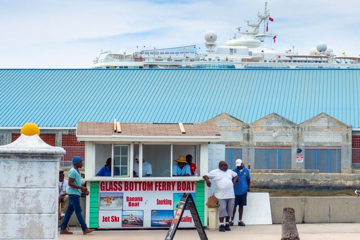 People gathering at a glass bottom ferry booth by the waterfront with a large ship in the background.
