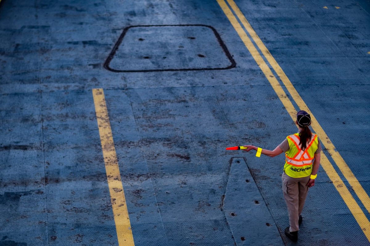 A BC Ferries worker directs traffic on the ferry deck, wearing a high visibility jacket.