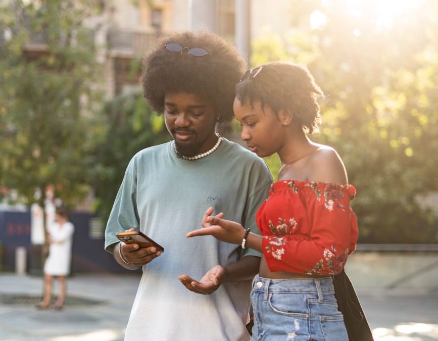 A young couple standing together at a bus stop, engaged with a smartphone in an urban setting, capturing a moment of connection and technology.