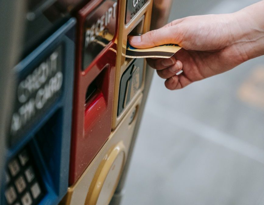 Close up of a hand inserting a metro card into a ticket vending machine in an urban setting.