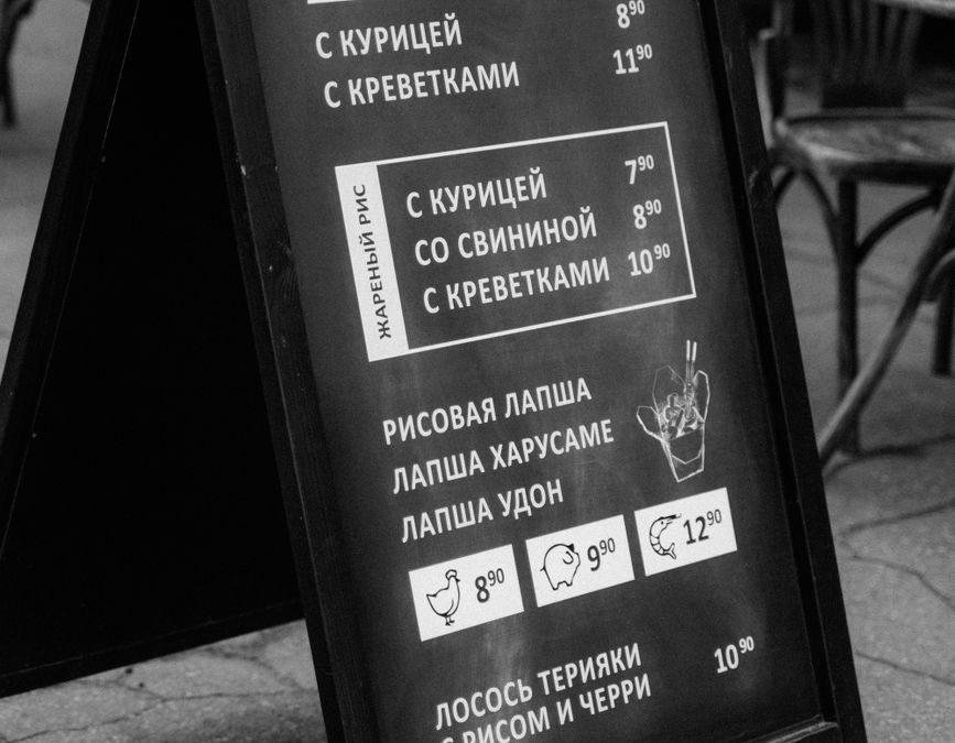 Monochrome photo of a restaurant menu board outdoors showcasing various dishes.