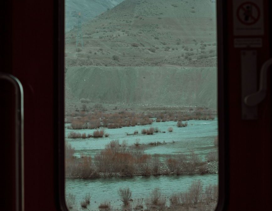 Peaceful mountain and river scene viewed through a train window.
