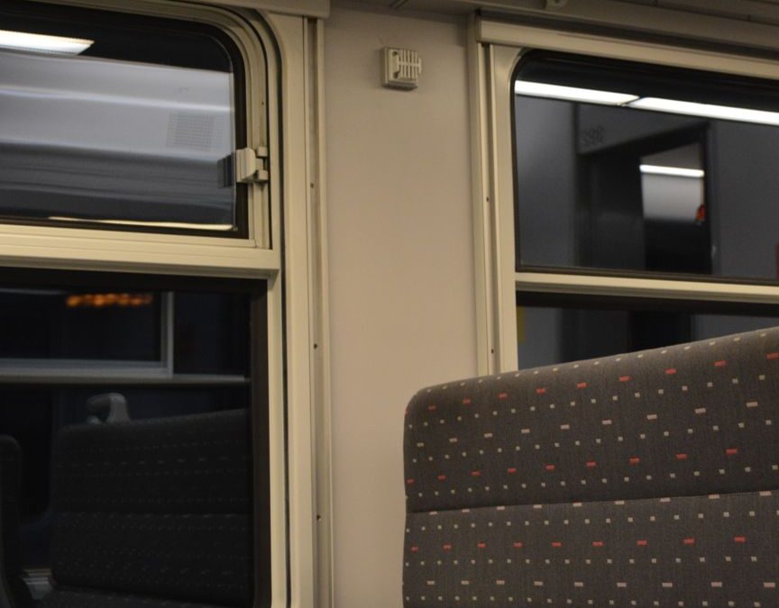 Empty train seat beside a window with a view of passing lights at night.