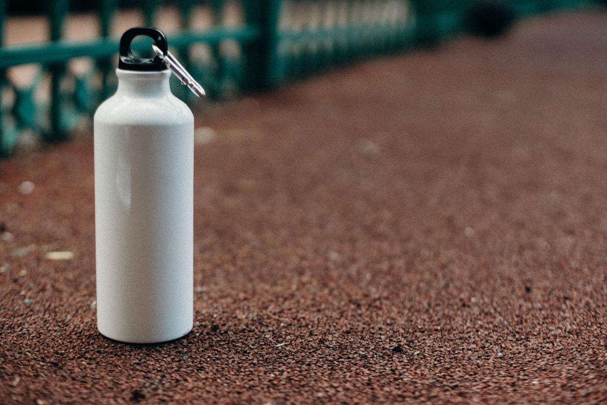 Close up of a white water bottle with carabiner on an outdoor track.