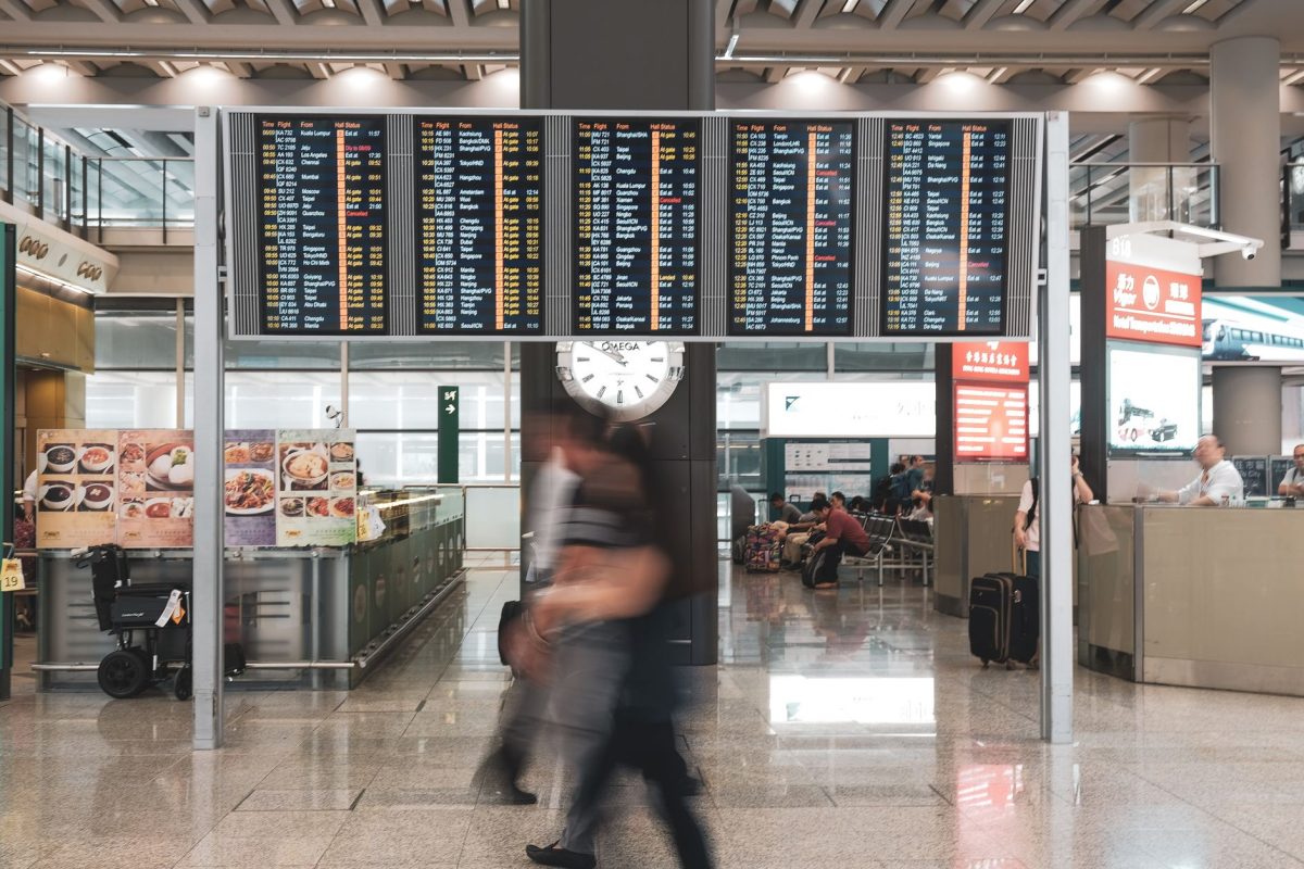 5 Bag Drop Details Travelers Often Learn Too Late at the Airport 1 Blurred motion of travelers in a modern airport terminal with departure screens and a prominent clock.