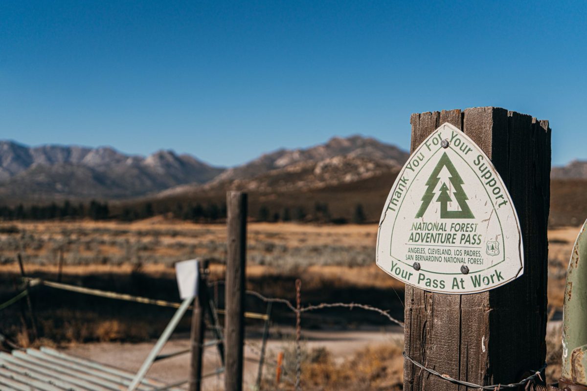 Close up of National Forest Adventure Pass sign on wooden post with mountains in the background.
