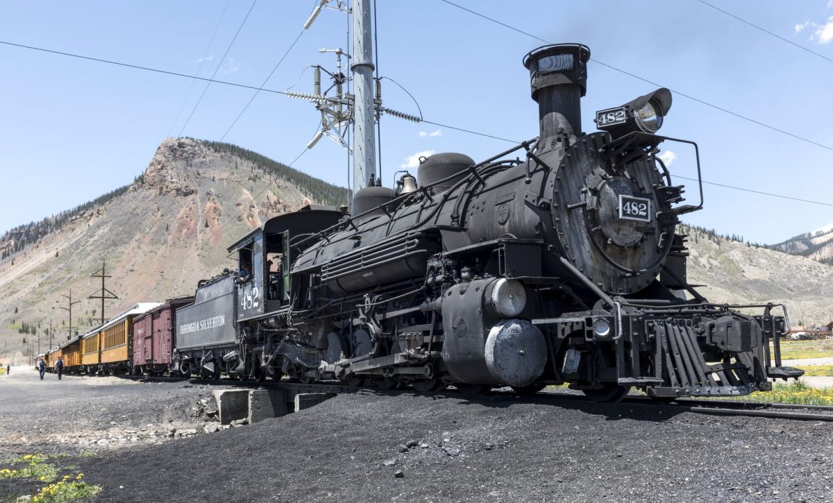 A historic steam locomotive travels through the scenic mountain landscape under a clear sky.