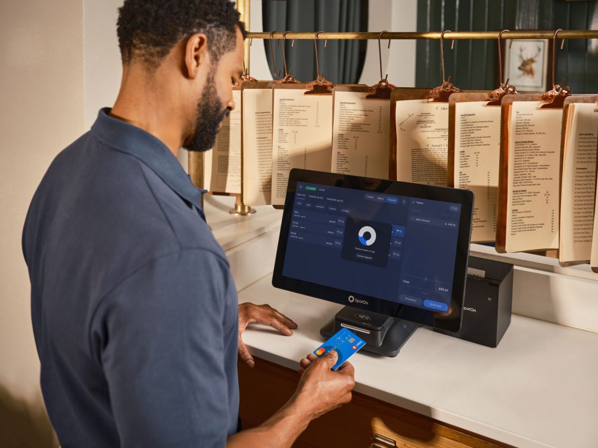 A restaurant staff member uses a POS system to process a credit card payment at the counter.