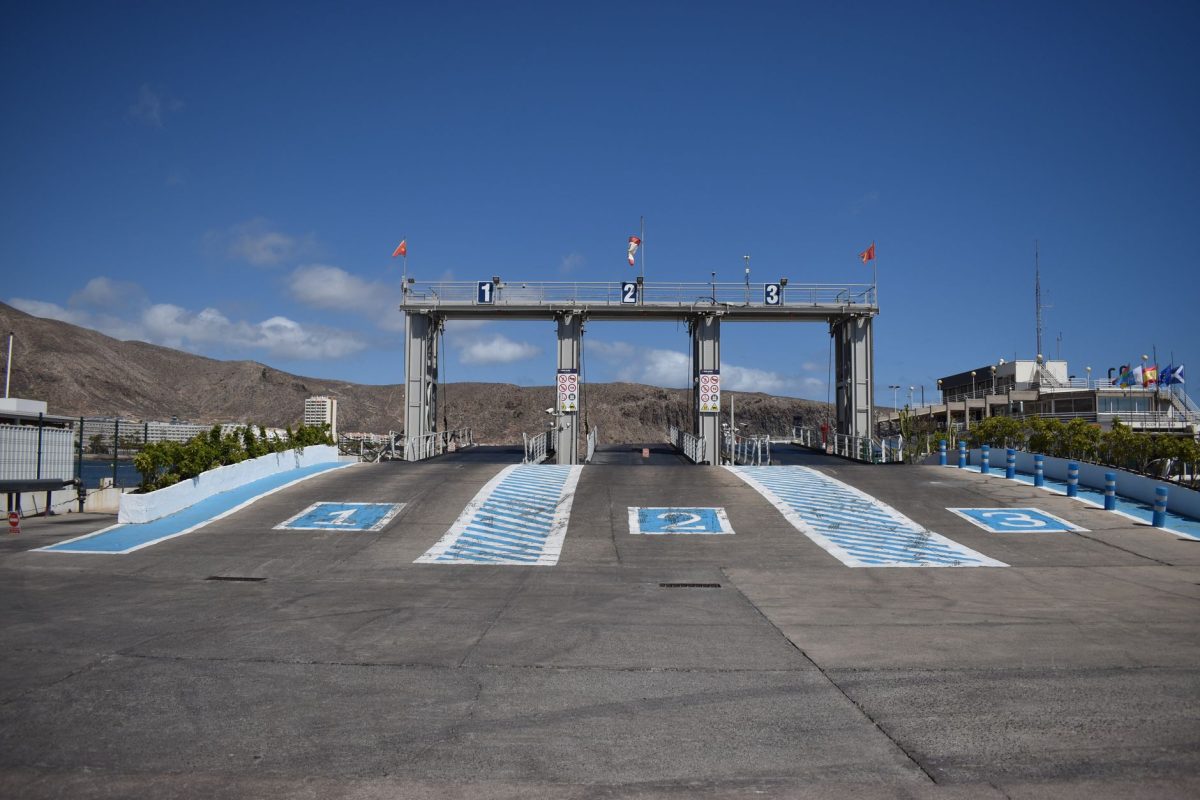 Ferry terminal ramp with numbered lanes, blue sky, and distant hills.