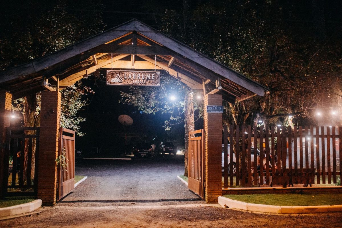Wooden arch with inscription and camp symbol on signboard above road with shiny lamps in twilight