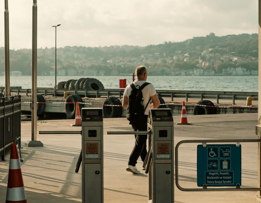 A man walks through gates at a ferry terminal with a harbor view. Urban setting.